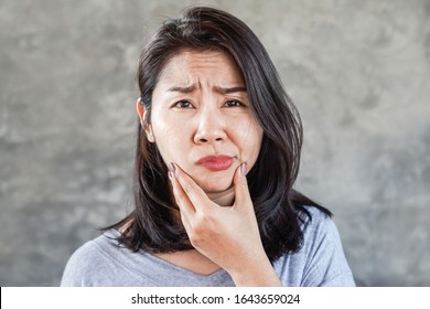 depressed Asian woman having problem with Bell's Palsy/Facial Palsy, hand holding her face 