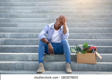 Depressed black guy with personal belongings sitting on stairs after losing his job, outside