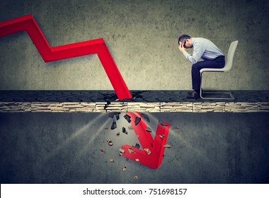 Depressed business man looking down at the falling red arrow going through a concrete floor. Fall and depreciation concept.