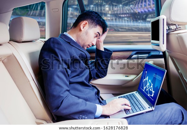 Depressed business person looking\
financial chart on laptop while sitting inside the\
car