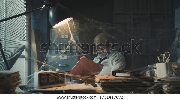 Depressed\
businessman dealing with business failure: he is sitting in his\
abandoned office and searching for\
paperwork