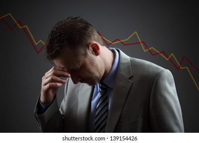 Depressed Businessman In Economic Crisis With Line Graph Showing Negative Trend
