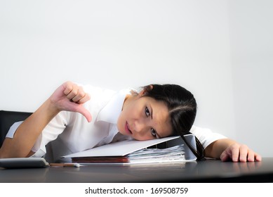 Depressed businesswoman giving a thumbs down to show that a business venture has been unsuccessful and a failure lying hunched over an office binder in depression
