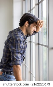 Depressed Caucasian Man Losing Job ,heartbroken, Alone, Feeling Bad And Expresses Negative. Unhappy Attractive Breaded Young Male Looks Outside Window In Living Room Interior Suffering Emotional Pain.