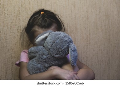 Depressed child sitting and hidden behind her toy teddy bear. domestic and violence, beaten sitting at the wall, Domestic violence. Copy space.