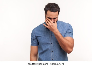 Depressed desparated man in blue shirt rubbing tired eyes, crying because of hopelessness and loneliness, nervous breakdown. Indoor studio shot isolated on white background
