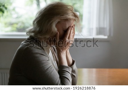 Depressed elder OAP 60s woman goes through crisis, loss, grief, dementia. Unhappy middle aged female pensioner covers face with hands in despair after receiving bad shocking news about health problem