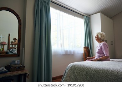 A depressed elderly widow sitting on her bed looking out the window - Powered by Shutterstock