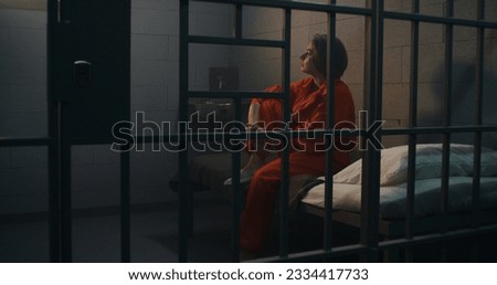 Depressed female prisoner, inmate in orange uniform sits on bed in prison cell. Woman criminal serves imprisonment term for crime in jail. Detention center or correctional facility. Justice system.