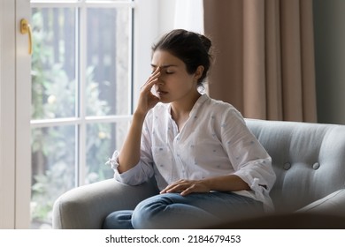 Depressed frustrated young Indian woman suffering from headache, migraine, touching face, head with closed eyes, feeling stressed, sick, tired, thinking over bad news, problems, crisis - Shutterstock ID 2184679453