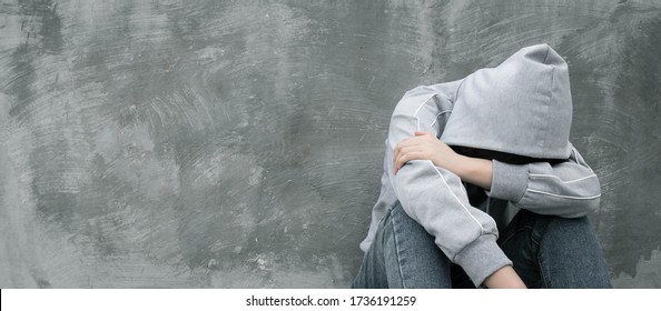 Depressed and hopeless teenage girl sitting alone after using drugs or drunk alcohol over grunge concrete wall. Drugs addiction and withdrawal symptoms concept. International Day against Drug Abuse.