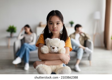 Depressed Japanese Adolescence Girl Hugs Toy. Offended Young Wife Ignores Husband, Sits On Sofa In Living Room Interior. Covid-19 Lockdown, Social Issues, Quarrel, Family Problems And Stress At Home