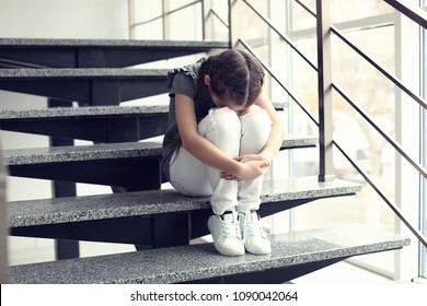 Depressed Little Girl Sitting On Stairs Indoors. Time To Visit Child Psychologist