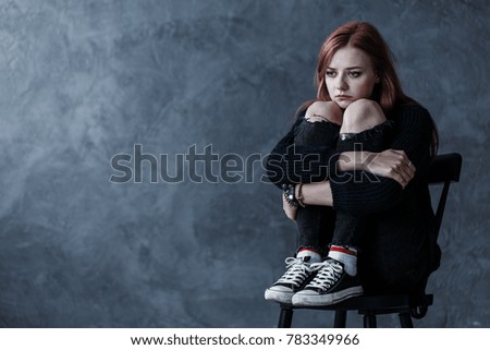 Depressed and lonely girl sitting on a chair against wall with copy space