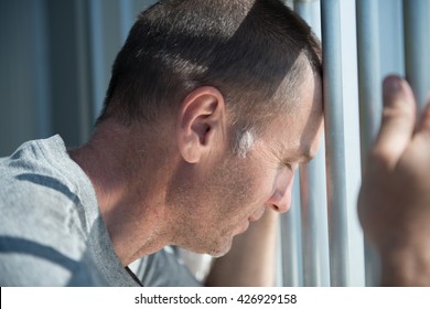 Depressed Male Inmate Holds Prison Bars In Despair