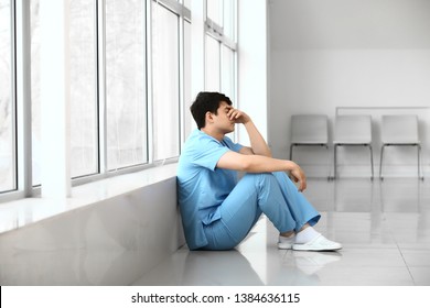 Depressed male medical assistant sitting near window in clinic - Powered by Shutterstock