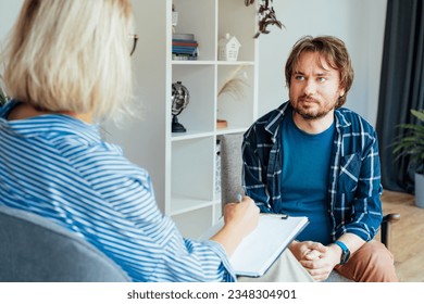 Depressed male patient having psychotherapy session with counselor at mental health clinic. Man with emotional problems consulting professional therapist i comfy office. Psychological help service. - Powered by Shutterstock