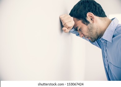 Depressed man with fist clenched leaning his head against a wall