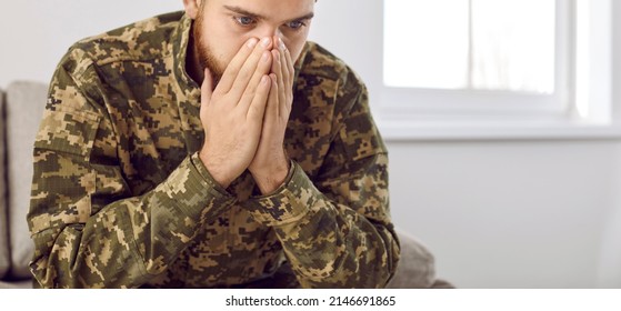 Depressed Man Recalling War Days. Portrait Of Veteran Soldier Who Has PTSD Sitting On Couch In Military Camouflage Uniform, Holding Hands On Face And Staring At Nothing Unable To Forget Horrors Of War