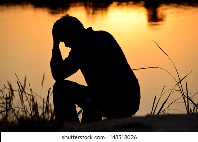 depressed man sitting against the light reflected in the water
