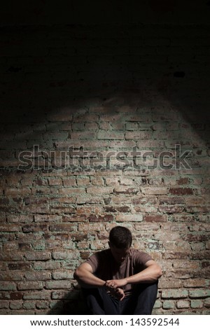 Depressed man sitting alone against brick wall.