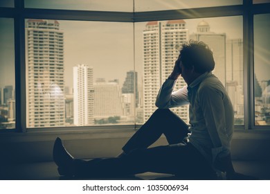 depressed man sitting head in hands on the interior Skyscraper with low light environment beside the windows over the cityscape background, dramatic concept - Shutterstock ID 1035006934