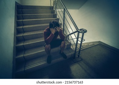 Depressed Man Sitting Head In Hands On The Staircase In The Fire Escape Or Building Stair With Low Light Environment, Dramatic Scene Concept