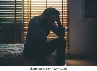 depressed man sitting head in hands on the bed in the dark bedroom with low light environment, dramatic concept