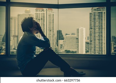 depressed man sitting head in hands on the interior Skyscraper with low light environment beside the windows over the cityscape background, dramatic concept - Shutterstock ID 663297736