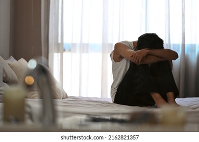 Depressed Man Sitting On The Bed In The Dark Bedroom With Low Light Environment. Negative Emotion And Mental Health Concept