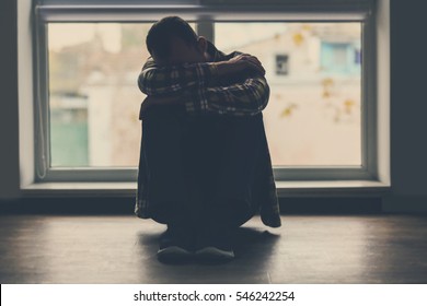 Depressed Man Sitting On Floor Near Window