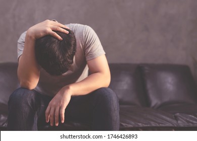 Depressed man sitting on the sofa and holding his forehead
