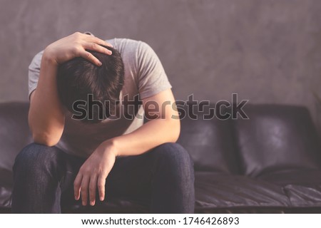 Depressed man sitting on the sofa and holding his forehead