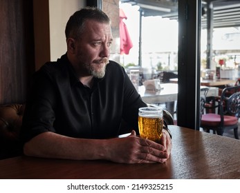 Depressed man sitting at the pub or bar table and drinking a glass of beer. - Powered by Shutterstock