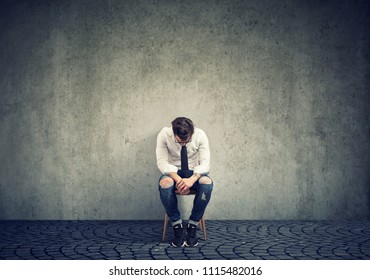 Depressed Man Upset With Bad Luck Sitting On Chair Alone Against Gray Background 