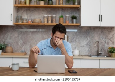 Depressed Man Working On Laptop In The Kitchen At Home. Distance Work Concept	