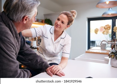 Depressed Mature Man In Dressing Gown Talking With Female Nurse In Kitchen At Home