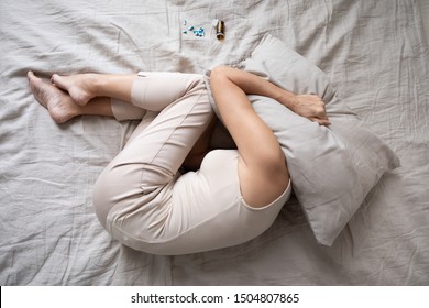 Depressed mature woman lying in bed with bottle of pills top view, covering head with pillow, unhappy older female suffering from insomnia or depression, psychological problem, overdose concept