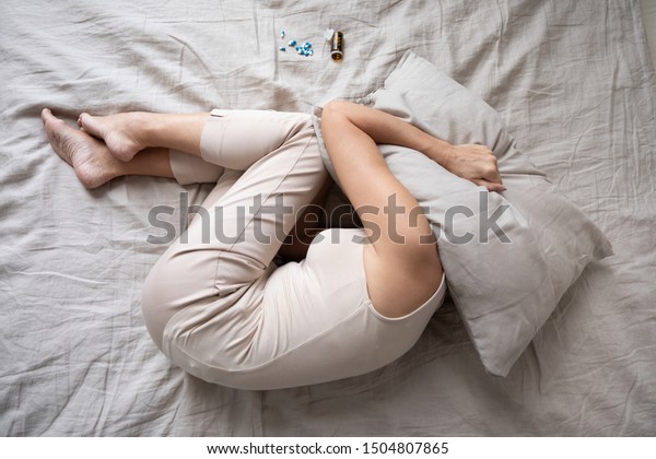 Depressed mature woman lying in bed with bottle\
of pills top view, covering head with pillow, unhappy older female\
suffering from insomnia or depression, psychological problem,\
overdose concept