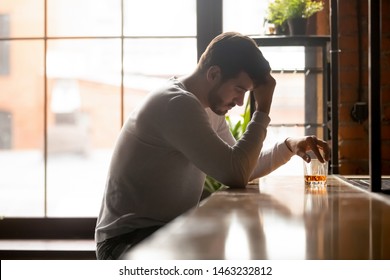 Depressed Millennial Man Sitting Alone At Bar Counter Drinking Strong Alcohol Thinking Of Relationships Problems, Stressed Sad Male Feel Despair Pondering Suffering From Alcoholism. Addiction Concept