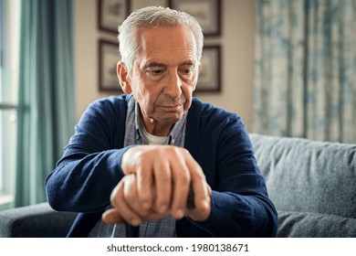 Depressed Old Man Sitting At Home While Holding Walking Stick. Retired Sad Man Holding Wooden Walking Cane Handle Sitting Alone At Care Facility. Elderly Man Suffering From Loneliness And Alzheimer.