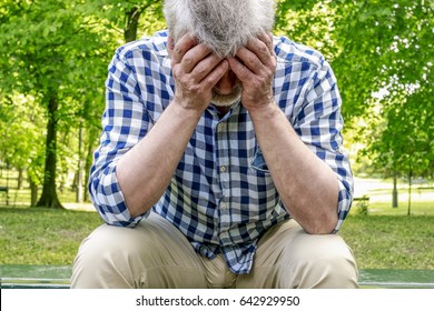 Depressed old man sitting on the bench in a park. 
