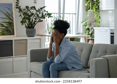 Depressed oppressed African American woman sits on couch in room waiting for psychologist flying psychological problems. Sad offended girl covering face with hands suffering from depression and stress - Shutterstock ID 2258138497