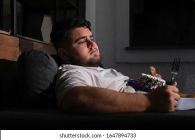 Depressed Overweight Man Eating Sweets In Living Room At Night