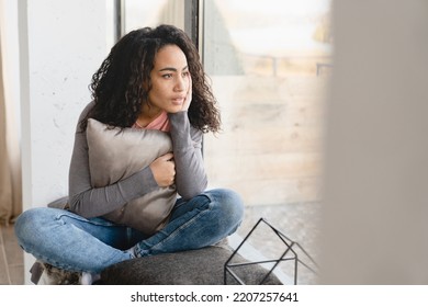 Depressed Pensive Thoughtful African Young Woman Housewife Suffering From Periods Pain Headache Coronavirus Migraine Broken Heart Looking Outside On Windowsill At Home On Self-isolation