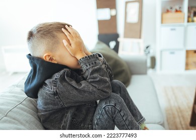 Depressed Sad Child Sitting On The Bed, At Home. Little Boy Is Hiding His Head Between Hands. Upset Problem Child With Head In Hands, Concept For Childhood Bullying, Depression Stress Or Frustration