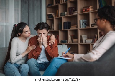 Depressed Sad Millennial European Wife Calming Husband With Doctor In Office Clinic Interior. Stress, Psychologist Support, Professional Help, Family Therapy, Relationship Problems, Grief And Pressure