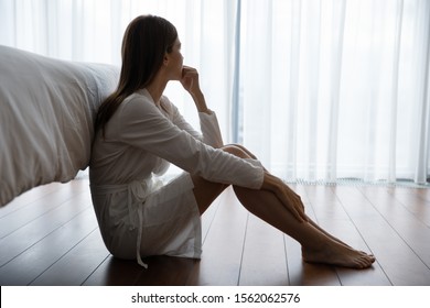 Depressed Sad Worried Young Woman Wear Night Gown Sit On Bedroom Floor Alone Troubled With Loneliness, Upset About Solitude Mental Problem Look At Window Think Of Abortion Regret Bad Mistake Concept