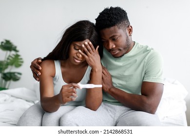 Depressed Sad Young Black Female And Male Upset Of Negative Pregnancy Test Result In Light Bedroom Interior, Copy Space. Husband Calms His Wife At Home. Infertility, Health Problems And Childlessness