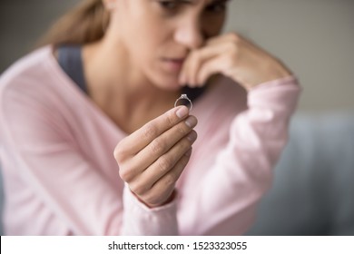 Depressed Sad Young Woman Wife Sit Alone Holding Engagement Wedding Ring In Hand Feeling Upset Disappointed Frustrated Unhappy Regret Marriage Mistake Suffer From Break Up Concept, Close Up View